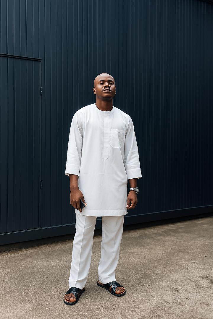 Man wearing a white outfit standing against a dark wall.